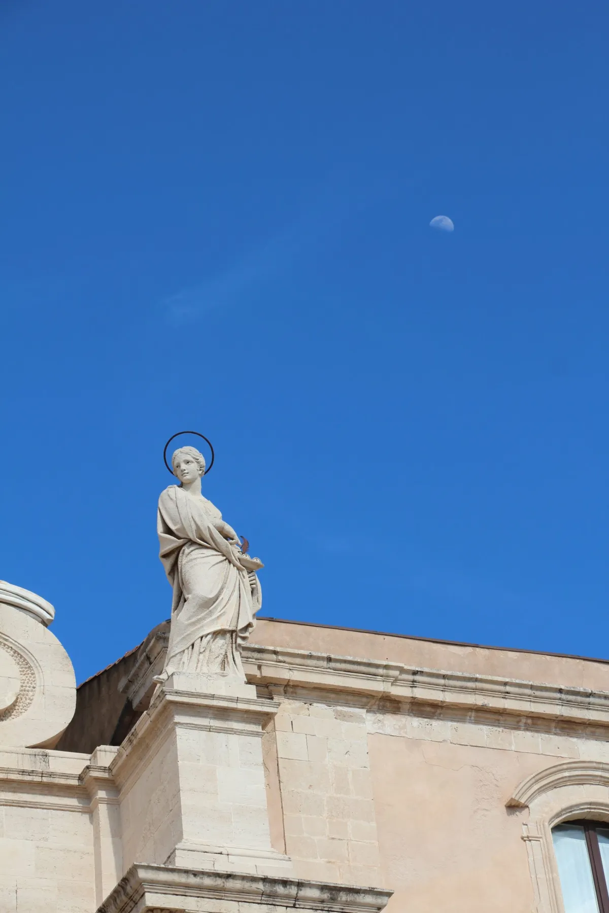 Statuie a unui sfânt cu aureolă, pe fundalul cerului albastru senin